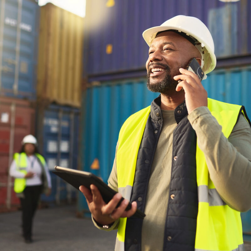 Man standing in front of shipping containers on the phone.